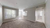 This single-floor residence offers a thoughtfully designed layout with a neutral color palette and clean finishes throughout. The open living area is anchored by plush carpeting, crown molding, and multiple windows with horizontal blinds that invite generous natural light. A pass-through counter connects the living space to the galley-style kitchen, which features white cabinetry, laminate countertops, a stainless steel sink, and black appliances including a refrigerator, range, microwave, and dishwasher. Light wood-look vinyl flooring runs through the kitchen and wet areas, providing a practical contrast to the carpeted living and sleeping spaces. The bedrooms are comfortably sized, with one room featuring a ceiling fan and a private window. A spacious walk-in closet with wire shelving offers ample storage. The bathrooms are finished with white vanity cabinetry, laminate counters, and wood-look flooring. One bathroom includes a tiled soaking tub with a shower combo, while another features a standalone shower. Crown molding in the main living areas adds a refined touch, and the overall design maintains a bright, understated aesthetic throughout.