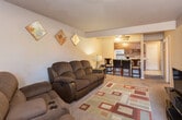 Located at 5A N Stonecrest Ct in Hobbs, New Mexico, this two-floor residence offers a practical and functional layout across its levels. The living room serves as the central gathering space, featuring wall-to-wall carpeting, a ceiling fan with light fixture, and an open sightline toward the kitchen and dining area. A patterned area rug anchors the space, and a window allows natural light to filter in.

The kitchen is equipped with white appliances, including a full-size refrigerator and range, complemented by dark wood cabinetry and light tile flooring. A bar-height dining counter with seating connects the kitchen to the living area, creating an open, casual flow between spaces.

The bedrooms are carpeted and include ceiling fans, windows with blinds for natural light and privacy, and sufficient space for standard furnishings. Each room maintains a neutral color palette that contributes to a calm, understated atmosphere.

The bathrooms feature tile flooring, dark wood vanity cabinetry, marble-style countertops with integrated sinks, chrome fixtures, and a shower-tub combination. The overall design throughout the home is straightforward and functional, with consistent finishes that lend a cohesive character to the space.