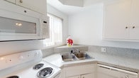 This two-story residence offers a clean, neutral design with a bright and airy atmosphere throughout. The main level features an open living area finished with light hardwood-style flooring, a textured ceiling, and a large sliding glass door that invites natural light and provides access to a balcony. A staircase with a white balustrade connects the two levels, contributing to the home's open, flowing layout. The kitchen is efficiently designed with white cabinetry, granite-style countertops, a double stainless steel sink, a coil-top electric range, built-in microwave, and a dishwasher — all finished in white for a cohesive look. A window above the sink allows natural light to brighten the workspace. The upper level hosts the bedrooms, each carpeted and finished with neutral white walls and textured ceilings. One bedroom features a wide mirrored sliding-door closet, while additional bedrooms are served by generous windows fitted with vertical blinds that diffuse natural light. The bathroom includes a full tub-shower combination, a vanity with granite-style countertops and white cabinetry, and light wood-style flooring, maintaining the home's consistent, clean aesthetic.