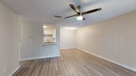 This single-floor unit offers a clean, modern aesthetic throughout, with light-toned luxury vinyl plank flooring that flows seamlessly across all living areas. The open living and dining space is bright and airy, featuring a textured ceiling, a ceiling fan with integrated lighting, and a pass-through window that connects directly to the kitchen—enhancing the sense of openness between the two areas. Track lighting adds a functional accent above the dining zone.

The galley-style kitchen is efficiently designed, offering white shaker cabinetry, a classic subway tile backsplash, dark countertops, a stainless steel sink, and a full suite of appliances including a range, microwave, dishwasher, and refrigerator. A flush-mount ceiling light keeps the space well-lit.

The bedroom is generously sized, with its own ceiling fan and large sliding glass doors fitted with vertical blinds, allowing abundant natural light and direct access to an outdoor area. A standard entry door also features in this room.

The bathroom is clean and functional, equipped with a full soaking tub and shower combination, a chrome curtain rod, and light wood-look flooring. Neutral wall tones throughout the unit create a cohesive, move-in-ready atmosphere.