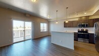 Located on the third floor at 1608 East South Riverton Avenue in Spokane, WA, Unit B-304 is a thoughtfully designed single-floor residence that blends modern finishes with functional living spaces. The entry foyer features durable wood-look flooring and leads directly into the open-concept main living area, where natural light pours in through multiple windows and a sliding glass door that opens to a private balcony with metal railing, offering pleasant outdoor views. The living and dining area flows seamlessly into the kitchen, which is equipped with rich dark-toned cabinetry, stainless steel appliances including a refrigerator, range, and microwave, and bright white countertops. A peninsula with pendant lighting serves as a central focal point, providing both additional prep space and a casual dining option. Track lighting and textured ceilings add character throughout the main living spaces. The bedroom is carpeted and filled with natural light from a large window, creating a calm and restful retreat. The bathroom features a dark wood vanity with a white countertop, a large mirror, and wood-look tile flooring, providing a clean and functional design. Throughout the unit, neutral tones and consistent finishes create a cohesive, move-in-ready atmosphere.