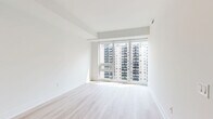 Located on the 19th floor at 3010 Tweedsmuir Ave in Toronto's Forest Hill neighbourhood, this well-appointed one-bedroom, one-bathroom unit offers a clean, modern aesthetic throughout. Light-toned hardwood flooring runs continuously across the space, complementing the crisp white walls and creating a bright, cohesive feel.

The open-concept living and kitchen area forms the heart of the unit. The kitchen is thoughtfully designed with flat-panel white cabinetry, tall built-in storage, a subway tile backsplash, stainless steel appliances including a full-size refrigerator and stove, and a peninsula countertop with an undermount sink — ideal for casual dining or food preparation. Track lighting above the kitchen adds focused illumination to the space.

The living area benefits from expansive floor-to-ceiling windows that flood the room with natural light and frame views of the surrounding Toronto skyline and neighbouring mid-rise buildings.

The bedroom is a well-proportioned, serene retreat featuring large windows with city views and a full-width mirrored sliding closet that enhances the sense of space and reflects natural light throughout the room.

The bathroom is finished with large-format beige floor tiles, full-height wall tiling in the tub surround, and a clean, functional layout with a soaker tub and shower combination.