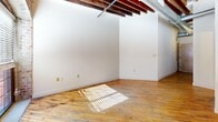 Located in Richmond, VA, this one-bedroom, one-bathroom loft at 1418 W Marshall Street showcases an impressive blend of industrial charm and contemporary design. The open layout is defined by striking exposed brick walls, rustic wood beam ceilings with visible ductwork, and warm hardwood floors that run throughout the main living areas, creating a cohesive and characterful aesthetic.

A hallway entrance leads into the main living space, where large windows allow natural light to pour in, illuminating the rich textures of the brick and wood overhead. The kitchen features light maple cabinetry extending to the ceiling for ample storage, dark countertops, a breakfast bar peninsula, and full appliances including a refrigerator, range, and built-in microwave. A stacked washer and dryer unit is conveniently tucked into a dedicated closet within the bedroom area.

The bedroom offers a cozy, well-defined retreat with continued hardwood flooring and access to the hallway and closet. The bathroom is finished with tile flooring and includes a full tub/shower combination. The space efficiently combines function and style, making it an ideal urban residence for those who appreciate loft-style living with historic architectural details.