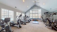 Located at 1400 Laurel Springs Dr in Durham, NC, this fitness center is a thoughtfully designed, single-floor facility built to support a comprehensive workout experience. The space is defined by its striking vaulted ceilings, which lend an open, airy quality throughout, while ceiling fans help maintain a comfortable environment during intense sessions.

Natural light pours in through an abundance of large multi-pane windows lining the walls, including a prominent bay window area fitted with a built-in padded bench — ideal for stretching or storing equipment such as the colorful medicine ball collection housed beneath it. The windows offer pleasant outdoor views, further enhancing the bright and motivating atmosphere.

The fitness floor is covered in durable carpet tile and is divided into functional zones. The cardio area is well-stocked with multiple treadmills, elliptical trainers, stationary bikes, and a rowing machine. The strength training zone features a robust selection of cable machines, multi-function weight stations, and a dedicated free weights area with a rack and adjustable bench. Full-length wall mirrors expand the sense of space and allow users to monitor their form during exercises.

Glass-paned French doors provide access to the space, and wall-mounted TVs add an entertainment element to cardio workouts. The overall ambiance is clean, modern, and functional — a well-rounded fitness facility suited for a variety of training styles.