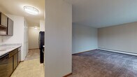 Located at 10145 W Cold Spring Rd in Greenfield, Wisconsin, this single-floor unit offers a practical and straightforward layout designed for comfortable everyday living. The interior is organized around an open flow between the kitchen and living areas, separated by a partial wall that defines each space while maintaining an connected feel throughout.

The galley-style kitchen features dark cabinetry, light granite-look countertops, tile flooring, and black appliances including an electric range and refrigerator, with a range hood overhead. A pass-through opening connects the kitchen directly to the adjacent dining or living area, where a ceiling fan and a window with blinds provide natural light and air circulation. Baseboard heating runs throughout the unit, ensuring consistent warmth.

The living spaces are finished with neutral-toned carpet and warm wood baseboards, creating a cohesive and understated aesthetic. The bedroom offers generous proportions, wall-to-wall carpet, and a wide louvered closet providing ample storage. The bathroom features a full soaking tub with a white tile surround and chrome fixtures, maintaining a clean and classic appearance. Overall, the unit presents a functional, move-in ready environment suited for a range of occupants.