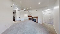 This two-story residence is defined by its dramatic, open-concept main living area, where soaring ceilings with bold yellow accent walls draw the eye upward and recessed lighting illuminates the generously sized, carpeted space. A wood-mantled fireplace serves as a focal point, adding warmth and character to the room. A curved spiral staircase with dark wood railings connects the main level to the upper floor, where an open loft-style landing features sloped ceilings, recessed lighting, and a dark wood railing overlooking the living area below.

The kitchen is well-appointed with rich dark wood cabinetry, stainless steel appliances including a range, microwave, and refrigerator, and a granite-topped island illuminated by pendant lights. Hardwood flooring grounds the space, and ample cabinet storage is provided throughout.

Additional rooms include a carpeted bedroom with a window offering natural light, a walk-in closet with built-in shelving and hanging rods, and a full bathroom featuring tile flooring, a tub-shower combination with tiled surround, a vessel sink vanity, and a large mirror. A dedicated laundry room houses a full-size washer and dryer alongside overhead cabinetry and tile flooring, offering practical convenience throughout the home.