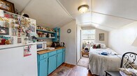Located on Pineapple Avenue in Melbourne, Florida, this compact studio is a single-floor space that makes efficient use of every square foot. The structure features a distinctive vaulted ceiling that adds a sense of openness and character throughout the interior. Rich hardwood-style flooring runs across the main living area, providing warmth underfoot and tying the space together visually.

The kitchen is a standout feature, outfitted with vibrant turquoise cabinetry topped with butcher block countertops that offer a pop of color and a rustic, functional charm. Open turquoise shelving above the counters provides additional storage and display space, while a full-size refrigerator and essential appliances ensure full functionality. The kitchen flows seamlessly into a modest dining area, where a small bistro-style table and chairs sit beneath the vaulted ceiling near the front entry door.

The sleeping area is tucked toward the rear of the space, benefiting from a large window that fills the nook with natural light and provides a pleasant outdoor view. The angled ceiling in this section echoes the overall architectural style of the structure. A bathroom completes the layout, offering all necessary amenities. The overall ambiance is cozy, eclectic, and full of personality, making this a uniquely charming space.