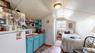 Located on Pineapple Avenue in Melbourne, Florida, this compact studio is a single-floor space that makes efficient use of every square foot. The structure features a distinctive vaulted ceiling that adds a sense of openness and character throughout the interior. Rich hardwood-style flooring runs across the main living area, providing warmth underfoot and tying the space together visually.

The kitchen is a standout feature, outfitted with vibrant turquoise cabinetry topped with butcher block countertops that offer a pop of color and a rustic, functional charm. Open turquoise shelving above the counters provides additional storage and display space, while a full-size refrigerator and essential appliances ensure full functionality. The kitchen flows seamlessly into a modest dining area, where a small bistro-style table and chairs sit beneath the vaulted ceiling near the front entry door.

The sleeping area is tucked toward the rear of the space, benefiting from a large window that fills the nook with natural light and provides a pleasant outdoor view. The angled ceiling in this section echoes the overall architectural style of the structure. A bathroom completes the layout, offering all necessary amenities. The overall ambiance is cozy, eclectic, and full of personality, making this a uniquely charming space.