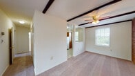 This single-floor residence offers a well-organized layout with a variety of distinctive architectural details. The living area is a standout space, characterized by dark exposed ceiling beams and a ceiling fan with a light fixture, adding both character and practicality. A full-height brick accent wall anchors one end of the living area, lending a warm, textured contrast to the otherwise neutral white walls. Decorative wrought iron railings delineate the transition between living zones, enhancing the open-concept feel of the space. Natural light flows in through multiple windows, and a set of sliding glass doors leads out to a private balcony with views of surrounding greenery.

The kitchen features warm-toned wood cabinetry, laminate countertops, and white appliances including a gas range, dishwasher, and refrigerator, all set over easy-care tile flooring. The bedrooms are carpeted and generously sized, with the primary bedroom offering dual closets with bifold doors. Additional bedrooms include their own closet storage. The bathroom is finished with white tile flooring, a full tub-shower combination, a windowed wall for natural light, and a vanity with ample counter space.
