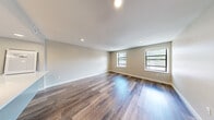 This single-floor residence offers 2 bedrooms and 3 bathrooms within a thoughtfully designed and efficiently organized layout. The combined kitchen and living room serves as the heart of the home, featuring rich hardwood-style flooring, recessed lighting, and multiple windows that bring in natural light. The kitchen is outfitted with modern gray cabinetry, white countertops, stainless steel appliances including a refrigerator and dishwasher, a deep single-basin sink, and a sleek range hood, all contributing to a clean, contemporary aesthetic. The living area extends generously, offering an open and airy feel. The primary bedroom is a comfortable, well-proportioned space with plush carpeting, while the second bedroom also features carpet and a large built-in closet with modern paneled doors for ample storage. The three bathrooms are finished with neutral tile work; one features a tub-shower combination, while another includes a glass-enclosed walk-in shower with large-format tile, a corner bench seat, and grab bars. A hallway connects the rooms efficiently, with a thermostat and utility panel conveniently accessible. The consistent neutral color palette throughout creates a cohesive and clean living environment.