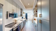 Located at 98 South River Drive in Tempe, Arizona, this efficiently designed one-bedroom, one-bathroom residence makes excellent use of its space through refined finishes and a cohesive aesthetic. The galley-style kitchen is a standout feature, showcasing custom blue-grey cabinetry with brushed gold hardware, under-cabinet lighting, white subway tile backsplash, and light granite countertops. Stainless steel appliances — including a range, dishwasher, and built-in microwave — complete the well-appointed cooking space. The open living area flows naturally from the kitchen, featuring warm hardwood-style flooring, a built-in media console, and open shelving with blue cabinetry accented by a distinctive gold pendant light. The generously sized bedroom offers a tray ceiling, a ceiling fan, large windows with deep navy curtains, and abundant natural light. The bathroom is elegantly finished with large-format tile flooring, a white vanity with gold hardware, granite countertops, wall sconce lighting, and a full tub-shower combination. A consistent palette of navy, white, grey, and gold ties each room together, creating a polished and inviting atmosphere throughout.