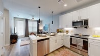 This single-story unit offers a thoughtfully planned layout that maximizes functionality across its compact footprint. The open-concept design seamlessly connects the kitchen and living room, creating a cohesive and social living environment. The kitchen is a standout feature, showcasing white shaker cabinetry, subway tile backsplash, stainless steel appliances including a refrigerator with ice maker, dishwasher, and range, as well as a peninsula island with seating for multiple guests and sleek pendant lighting overhead. Light wood-style flooring runs throughout the main living areas, adding warmth to the contemporary aesthetic.

The living room benefits from large windows that invite abundant natural light and features a ceiling fan. A hallway connects the main living area to the private spaces, where an in-unit stacked washer and dryer are conveniently located. The bedroom is carpeted, receives natural light through a sizable window, and includes a ceiling fan. The full bathroom is cleanly appointed with a white vanity and direct access to a walk-in closet with built-in shelving and hanging rods. Recessed lighting and a neutral color palette throughout contribute to a bright, modern ambiance.