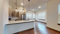 Located at 3215 Hill St NW in Duluth, GA, this well-appointed single-floor residence offers a thoughtfully designed open-concept layout with modern finishes throughout. The kitchen is a standout feature, showcasing light wood cabinetry, a herringbone tile backsplash, stone countertops, a large peninsula with an undermount sink, and a full suite of stainless steel appliances. Elegant pendant lighting hangs above the peninsula, adding warmth to the space. The kitchen flows seamlessly into the living area, which is bathed in natural light from multiple windows fitted with blinds, all set over rich hardwood-style flooring. A hallway with recessed lighting connects the main living areas to the private quarters. The bedrooms are carpeted for comfort, each featuring large windows that invite natural light and access to ample closet space, including a walk-in closet in the primary bedroom. The primary bathroom is generously proportioned, offering a dual-sink vanity with stone countertops, a glass-enclosed shower, and large-format tile flooring. A secondary bathroom provides a vanity with stone countertops and overhead cabinetry. The overall aesthetic is clean, contemporary, and move-in ready.