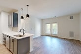 Located at 13525 Grayson Hill Cir in Dale City, VA, this single-floor, three-bedroom, two-bathroom home offers a clean, modern aesthetic throughout. The open-concept kitchen and living area serves as the heart of the home, featuring gray shaker-style cabinetry, stainless steel appliances, a white quartz peninsula with a black matte faucet and undermount sink, and dual pendant lights overhead. Light wood-look flooring extends across the main living areas, enhancing the bright, airy feel of the space. The living room is bathed in natural light thanks to French doors that open to an outdoor area, creating a seamless indoor-outdoor connection. A dedicated entry area with crisp white walls provides a welcoming transition into the home. The three bedrooms are carpeted for comfort, with the primary bedroom offering a generous footprint. The bedrooms feature ample wall space and are served by two full bathrooms, each finished with gray vanity cabinetry, white countertops, wood-look flooring, and matte black hardware and fixtures. A hallway connects the bedrooms and bathrooms, and a closet provides additional storage. Throughout, white walls and consistent finishes create a cohesive, contemporary atmosphere.