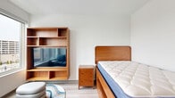 Located at 2132 Stokes Blvd in Cleveland's University Circle neighborhood, this efficiently designed one-bedroom, one-bathroom unit makes excellent use of its compact footprint. Light wood-look flooring runs throughout, lending a clean, cohesive aesthetic to the entire space.

The open living area connects seamlessly to a modern kitchen outfitted with gray cabinetry, a stainless steel refrigerator, built-in microwave, and white countertops. A large window at the living end of the unit fills the space with natural light while offering views of the surrounding Cleveland cityscape.

The bedroom is furnished with warm walnut-toned pieces, including a platform bed, a matching nightstand, and a built-in shelving unit with an integrated media center. A colorful area rug and a stacked pouf add a touch of personality to the space.

A stacked washer and dryer unit is conveniently tucked behind a closet door, providing in-unit laundry without sacrificing valuable living space. The bathroom features a clean, contemporary design with a gray vanity, white countertop, large mirror, a tub-shower combination, and matte black hardware and grab bar accents throughout.

Overall, the unit presents a modern, functional design well-suited for urban living in Cleveland, OH.
