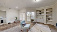 This single-floor space offers a well-organized layout designed for comfortable everyday living. The living area serves as the heart of the home, featuring crown molding, recessed lighting, and a mix of wood-look and carpeted flooring. Large windows dressed with white horizontal blinds allow generous natural light to fill the room, while a set of French doors provides additional brightness and outdoor access. A built-in shelving unit with lower cabinetry adds both storage and a refined architectural detail to the space.

The kitchen is outfitted with ample white cabinetry, light speckled countertops, and a full suite of white appliances including a range, dishwasher, and built-in microwave. Wood-look flooring runs underfoot, contributing to a clean, cohesive aesthetic throughout the functional workspace.

The bathroom features an extended vanity with white cabinetry, a wide mirror, and a multi-bulb light bar overhead, offering plenty of counter space and storage. Wood-look flooring continues here, reinforcing the consistent design language of the home.

An entry area with tile flooring and panel-style doors completes the layout, providing a practical transition point into the main living spaces. Overall, the space presents a light, neutral palette with functional finishes throughout.