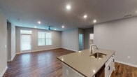 This single-story residence offers three bedrooms and two bathrooms within a well-designed, open-concept layout. The kitchen serves as the centerpiece of the main living area, featuring a large island with a undermount sink and quartz countertops, white shaker-style cabinetry with brushed hardware, subway tile backsplash, and a full suite of stainless steel appliances including a refrigerator, range, microwave, and dishwasher. The kitchen flows seamlessly into the living area, which is illuminated by recessed lighting and a ceiling fan, with windows allowing natural light to fill the space. Rich, wood-look plank flooring runs throughout the main living areas and bedrooms, complementing the neutral gray walls. The primary bedroom is generously sized with a ceiling fan and direct access to a private bathroom, which includes a single-sink vanity with quartz countertops and white cabinetry. The secondary bathroom features a tub-shower combination with white subway tile surround, a matching vanity, and wood-look flooring. The additional bedrooms offer comfortable proportions, with one featuring soft carpet and another with hard flooring, both served by recessed or ceiling-mounted lighting.