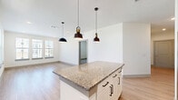 This well-designed two-bedroom, two-bathroom residence offers a thoughtful single-floor layout that maximizes functionality and comfort. The open-concept kitchen and living area serves as the heart of the home, anchored by a large central island topped with speckled granite countertops and illuminated by striking matte black pendant lights. The kitchen is fully equipped with stainless steel appliances, including a French door refrigerator, range, microwave, and dishwasher, all complemented by crisp white shaker cabinetry, subway tile backsplash, and a deep undermount sink. Light wood-look flooring flows throughout the main living areas, creating a bright and airy atmosphere enhanced by natural light from multiple windows. A well-proportioned hallway connects the living spaces to the private quarters, with two closets providing ample storage. The bedrooms feature plush carpeting, offering a comfortable retreat, while each bathroom is appointed with white vanity cabinetry, granite countertops, and large mirrors. The primary bedroom provides a generously sized layout with its own dedicated closet space. Clean white walls, recessed lighting, and consistent finishes throughout lend the space a cohesive, modern aesthetic suited for everyday living.