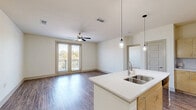 Located in Corinth, TX, this single-story residence offers a thoughtfully designed layout across two bedrooms, two bathrooms, and multiple closets. The open-concept kitchen and living area serves as the heart of the home, anchored by a large central island with a quartz countertop, undermount sink, and elegant pendant lighting. Light wood cabinetry pairs with stainless steel appliances, including a refrigerator, range, and microwave, while track lighting illuminates the kitchen workspace. Wood-look flooring runs throughout the main living areas, enhancing warmth and continuity. The living room benefits from abundant natural light through large windows and glass patio doors fitted with blinds, leading to a private outdoor patio. A ceiling fan adds comfort to both the living room and each bedroom. The bedrooms feature plush carpeting and dedicated closets, with the primary bedroom offering access to a well-appointed en-suite bathroom complete with a soaking tub, tiled surround with decorative accent banding, and wood-look flooring. The second bathroom mirrors a similarly clean, functional design. A hallway connects the spaces efficiently, and an in-unit laundry area adds everyday convenience to this move-in-ready home.