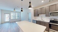 This single-story, 2-bedroom, 2-bathroom residence in McDonough, Georgia offers a thoughtfully designed open-concept layout that maximizes functionality. The kitchen and living area flow seamlessly together, anchored by a large white quartz island that serves as both a workspace and gathering point. The kitchen features dark taupe cabinetry, a classic subway tile backsplash, stainless steel appliances including a range, microwave, dishwasher, and refrigerator, and a recessed double sink. Two stylish pendant lights hang above the island, while recessed lighting illuminates the full kitchen. Light wood-look flooring runs throughout the main living areas, and a ceiling fan is installed in the living room, which also provides access to an exterior door flanked by large windows that bring in generous natural light.

The primary bedroom is a comfortable size with plush carpeting and features a walk-in closet outfitted with multi-tier wire shelving. The second bedroom, also carpeted, includes a window with exterior views. Both bathrooms offer dark cabinetry and wood-look flooring, with one bathroom featuring a tiled tub-shower combination. A dedicated laundry room accommodates a full-size washer and dryer.