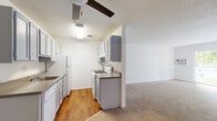 Located at 8712 S 87th Ter in Justice, IL, this single-floor residence offers a straightforward and practical layout designed for comfortable everyday living. The kitchen is a galley-style space finished with warm hardwood-style flooring, gray cabinetry providing ample storage, laminate countertops, and white appliances including a gas range and refrigerator. A ceiling fan with a built-in light fixture overhead and a textured ceiling add functional detail to the kitchen area, which opens toward the adjoining living space. The living and bedroom areas are finished with wall-to-wall carpet in a neutral tan tone, creating a warm and cohesive feel throughout. Crisp white walls and textured ceilings carry through these rooms, while baseboard heating units run along the lower walls, ensuring efficient climate control. The bedroom benefits from a window that allows natural light and offers a view of surrounding greenery. The bathroom features a single-sink vanity with gray cabinetry, brushed nickel fixtures, a mirror cabinet, and a tiled tub-shower combination. Overall, the space presents a clean, functional, and well-organized interior suited for residential living.
