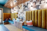 Located at 100 Oakbrook Drive in McDonough, GA, this single-floor space delivers a striking blend of contemporary design and playful artistic expression. The main corridor serves as an inviting reception and lounge area, anchored by a teal-painted ceiling that contrasts beautifully with warm wood accents and globe pendant lighting. Underfoot, a distinctive terrazzo tile floor runs through the main hall, transitioning to vibrant yellow carpet in the office rooms, adding energy and visual contrast throughout.

The lounge area features a built-in banquette with teal upholstered seating and a bold gold channeled-velvet backrest, set against an eye-catching abstract wood-tone wallcovering illuminated by globe sconces. A built-in wood and marble-topped counter provides functional workspace within the lounge. Natural light pours in through glass entry doors, offering views of the surrounding exterior.

Two private office rooms are wrapped in striking black-and-white line-art face wallpaper, lending each space a distinctive artistic character. The offices are furnished with sleek dark desks, modern pendant lighting, and contemporary seating, with windows providing natural light and outdoor views. Together, these spaces offer a cohesive, design-forward environment ideal for focused work or private meetings.