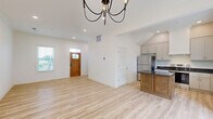 This two-story home offers a thoughtfully laid-out floor plan across two evenly divided levels, combining modern finishes with a clean, bright aesthetic throughout. Light-toned hardwood-style flooring flows consistently through the main living areas, complementing the crisp white walls and recessed lighting found in every room.

The first floor hosts the open-concept living, dining, and kitchen area. The kitchen is well-appointed with white shaker cabinetry, dark granite countertops, stainless steel appliances including a refrigerator and dishwasher, and a GE electric range. A chandelier anchors the living and dining space, while vaulted ceiling detail and a wood-framed front door add architectural character. A hallway with a louvered utility door provides additional storage access.

Upstairs, three bedrooms offer natural light through blinds-fitted windows. The primary bedroom is notably spacious, featuring a walk-in closet, an additional closet, and a stylish barn door accent. Each of the three bathrooms is finished in white with undermount sinks, shaker-style vanities, and large mirrors.

A standout feature is the expansive covered second-floor balcony, finished with a warm wood-plank ceiling and white railings, offering sweeping views of the surrounding greenery and open landscape.