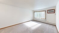 Located at 3434 Highlander Dr in Eagan, Minnesota, this single-floor residence offers a straightforward and functional layout. The floor plan, as revealed by a 3D overview, arranges the living space, kitchen, and bathroom in a compact, efficient configuration.

The living area is bright and open, featuring neutral wall-to-wall carpeting and white walls that create a clean, versatile backdrop. A large window fitted with vertical blinds allows natural light to stream in, casting sunlight across the floor and offering views of surrounding greenery. A baseboard heating unit runs along the exterior wall, providing warmth throughout the space.

The galley-style kitchen is lined on both sides with warm oak cabinetry offering generous storage above and below the countertops. White appliances, including an electric range, refrigerator, and dishwasher, are neatly integrated alongside a double-basin sink. Tile-style flooring adds durability to the space.

The bathroom is clean and functional, featuring a full tub-shower combination with grab bars, a toilet, and a single-sink vanity with oak cabinetry and a large wall mirror. Tile-style flooring completes the room. Additional carpeted spaces provide flexibility for bedroom or multipurpose use, all finished with consistent wood baseboards throughout.