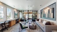 This single-floor amenity space is a masterclass in contemporary interior design, offering a variety of thoughtfully appointed areas that balance function and sophistication. The main lounge area features plush seating, bold artwork, and distinctive carved wood coffee tables anchored by a patterned area rug. A circular green velvet settee and dramatic geometric-patterned accent wall define a stylish gathering rotunda, while a coffered ceiling detail and gold chandelier add architectural elegance overhead. Adjacent, a game room impresses with soaring vaulted ceilings, exposed dark wood beams, herringbone hardwood flooring, a stone-clad fireplace, and a regulation-size pool table. Deep emerald green banquette seating lines the wall beneath decorative geometric panels, creating intimate lounge nooks. The gourmet kitchen showcases a sprawling marble island with bar seating, floor-to-ceiling marble backsplash, dark cabinetry with glass-front displays, and a trio of cascading glass pendant lights. A dedicated workspace features sliding steel-and-glass barn doors that open to a private conference and seating area with natural light and warm wood wall paneling. Together, these areas create a cohesive, upscale environment ideal for work, socializing, and leisure.