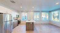 Located at 9950 NE Gibbs Dr in Hillsboro, Oregon, this well-appointed 2-bedroom, 2-bathroom residence offers a thoughtfully designed single-floor layout. Light wood-tone flooring runs throughout the entire space, creating a cohesive and clean aesthetic.

The heart of the home is an open-concept kitchen, dining, and living area filled with natural light from multiple large windows fitted with white horizontal blinds. The kitchen features white upper cabinetry, walnut-toned lower cabinets, a subway tile backsplash, stainless steel appliances including a refrigerator, range, and microwave, and a central island with a white quartz countertop and undermount sink. A balcony door off the living area provides outdoor access and additional views of the surrounding neighborhood and greenery.

A bright hallway connects the living areas to the two bedrooms, both of which are generously sized with large windows that invite natural light. The primary bedroom is spacious with a dedicated closet. Both bathrooms are finished in a clean, modern style, with one featuring a walk-in shower with bench seating and white tile surround.

A dedicated laundry room houses a stacked Whirlpool washer and dryer alongside built-in wire shelving for additional storage. The entrance and a separate closet round out this functional, contemporary home.