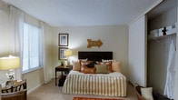 Located at 10725 Abercorn Ext in Savannah, Georgia, this single-floor residence offers a welcoming and comfortable living environment in a well-established area of the city. The home is designed with a warm, coastal-inspired aesthetic that reflects the charm of its Southern surroundings.

The bedroom is a standout feature of the space, showcasing soft, neutral-toned walls that create a calm and restful atmosphere. Plush wall-to-wall carpeting adds to the comfort underfoot, while large windows dressed with elegant white curtains allow natural light to filter in gently throughout the day. The room features a textured ceiling, contributing a classic residential character to the space.

Warm decorative touches — including framed coastal artwork, a wooden bedside table with a soft-glow lamp, and cheerful accent pillows in earthy tones of orange, green, and brown — give the bedroom a cozy, lived-in feel. A closet integrated along one wall provides practical storage while maintaining the room's clean lines.

Overall, the space exudes a relaxed, beach-inspired warmth that is both inviting and functional, making it well-suited for comfortable everyday living in the heart of Savannah.