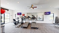Located at 307 Willow Manor Dr in O'Fallon, Missouri, this well-appointed community fitness center offers a thoughtfully designed single-room workout space with a clean, modern aesthetic. The interior features neutral-toned carpet flooring, crisp white walls, and recessed lighting complemented by a ceiling fan that helps maintain a comfortable environment during workouts.

The space is equipped with a comprehensive selection of cardio and strength training equipment, including multiple treadmills, an elliptical trainer, a recumbent bike, and an upright stationary bike. A multi-functional cable machine and a dedicated weight rack with dumbbells provide ample options for strength training. TRX suspension straps and stability balls round out the functional fitness offerings.

A large wall-to-wall mirror along one side of the room enhances the sense of openness while allowing users to monitor their form. Multiple wall-mounted flat-screen TVs provide entertainment during workouts. A water fountain is conveniently accessible near the entrance area.

Natural light filters in through several windows, including views of the surrounding residential community. Glass-panel doors connect the fitness center to an adjacent community room and provide direct access to the outdoor area. The space maintains a polished, community-focused atmosphere suited for a broad range of fitness routines.