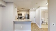 Located at 151 Beecroft Road in North York, Toronto, this one-bedroom, one-bathroom unit offers a thoughtfully designed layout making efficient use of its space. The open-concept kitchen and living area serves as the heart of the unit, featuring a peninsula with a light stone countertop and undermount sink that separates the kitchen from the living space. The kitchen is equipped with stainless steel appliances, including a refrigerator, electric range, and built-in microwave, complemented by white cabinetry with subway tile backsplash and track lighting overhead. Light wood-tone laminate flooring flows throughout the unit, adding warmth and continuity. The living area benefits from a sliding glass door that opens onto a private balcony, allowing natural light to fill the space and offering views of the surrounding neighbourhood. The bedroom is a well-proportioned room with a window overlooking the cityscape, neutral toned walls, and a sliding-door closet providing ample storage. The bathroom is finished in clean white tiling and includes a full soaker tub with shower. The overall aesthetic is modern and neutral, with a consistent palette of whites and warm greys creating a bright, cohesive interior throughout.