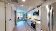 Located at 2801 Sunset Place in Los Angeles, this single-floor unit offers a thoughtfully designed open-concept layout that seamlessly blends living, dining, and sleeping areas. The space is characterized by light wood-tone flooring, clean white walls, and an abundance of natural light streaming through large windows that frame views of the surrounding Los Angeles cityscape and palm trees.

The kitchen runs along one wall in a galley-style configuration, featuring white and light wood cabinetry, white quartz countertops, stainless steel appliances including a range, microwave, dishwasher, and refrigerator, plus a stacked washer and dryer conveniently tucked behind louvered closet doors nearby.

The living and sleeping areas share an open, airy space defined by bold, contemporary artwork and eclectic furnishings. A sculptural white console with arched cutouts supports a large circular gold-framed mirror, adding an artistic focal point. Colorful accent pillows and layered rugs contribute warmth and personality throughout.

The bathroom features light tile flooring, a full soaking tub with shower, warm wood vanity cabinetry, and a clean, minimalist aesthetic. The overall ambiance is modern and vibrant, blending contemporary design with expressive, curated décor.