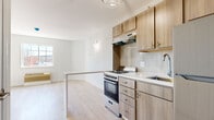 Located at 1151 E Main St in Meriden, Connecticut, this single-floor residence showcases a clean, contemporary design with light hardwood flooring throughout, creating a bright and cohesive aesthetic across every room.

The open-concept kitchen is a standout feature, outfitted with warm-toned wood cabinetry, brushed nickel hardware, a white quartz peninsula countertop, a gas range with stainless steel appliances including a refrigerator, a single-basin sink, and a textured tile backsplash. A stylish pendant light fixture anchors the space, while the peninsula provides a natural division between the kitchen and the living area. The living space benefits from natural light streaming through a multi-pane window with views of the surrounding landscape.

The bedroom is generously proportioned, featuring light-washed hardwood floors, a rich dark accent wall with a textured finish, and direct access to the bathroom. Natural light fills the room through well-positioned windows.

The bathroom is elegantly appointed with large-format dark marble-style floor tiles, a combination tub and shower, a wall-mounted vanity with a white countertop and integrated sink, a backlit mirror, and a decorative 3D-textured tile wall that adds a sophisticated touch.

Overall, this residence offers a modern, move-in-ready living environment with quality finishes and a functional layout.
