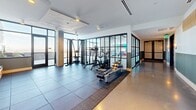 Located on Blake Street in Denver's vibrant 80205 neighborhood, this fitness center is designed to support a full spectrum of workout routines within a spacious, thoughtfully organized layout. The facility is divided into distinct zones, each tailored to specific training needs.

The main strength training area features large-format tile flooring and is outfitted with a variety of cable machines, multi-use functional racks, adjustable benches, and a comprehensive free weights section with organized dumbbell storage. Full-length mirrors line portions of the walls, aiding in form and technique. Recessed and ambient lighting throughout creates a clean, well-lit environment.

A dedicated cardio zone transitions into a separate area with polished concrete flooring, housing treadmills, stationary bikes, rowing machines, and stair climbers. Built-in open shelving provides convenient storage for personal items and accessories, while a wall-mounted display screen adds a modern touch.

Floor-to-ceiling glass partitions and large windows in key areas allow natural light to filter through, providing views of the surrounding Denver skyline. The industrial-inspired ceiling, featuring exposed concrete elements and dark structural beams, ties together the contemporary aesthetic. Rubber mat flooring in high-use zones offers both safety and durability throughout the facility.