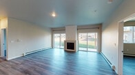 This well-appointed single-floor unit offers a thoughtfully designed open-concept layout finished with durable wood-look flooring that flows seamlessly throughout every room. The spacious living area is a standout, featuring a centrally positioned fireplace flanked by two sliding glass doors that fill the room with natural light and provide views of the surrounding greenery. Baseboard heating and a wall-mounted mini-split HVAC unit ensure year-round comfort.

The kitchen is outfitted with white shaker-style cabinetry, granite countertops, a central island with sink, and a full suite of stainless steel appliances including a French door refrigerator, electric range, microwave, and dishwasher. The kitchen connects smoothly to the main living and dining areas, making it ideal for entertaining.

The bedrooms are generously sized, with one featuring a ceiling fan and a large window overlooking the exterior. Additional rooms offer ample wall space and easy access to shared hallways. A dedicated laundry closet with an in-unit washer is conveniently located off the main living area.

The bathrooms are finished with white vanity cabinetry, granite countertops, large mirrors, and wood-look flooring. The full bath includes a tub-shower combination, while a second bath provides a walk-in shower. The unit's neutral color palette and modern finishes create a clean, inviting atmosphere throughout.