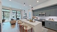This thoughtfully designed single-story residence offers 1,160 square feet of living space across 2 bedrooms, 2 bathrooms, a dedicated office, and a full laundry room. The open-concept kitchen and living area serves as the heart of the home, where sage-green shaker cabinetry, quartz countertops, a large center island with an undermount sink, and stainless steel appliances define a sleek, functional kitchen. Pendant lighting and recessed fixtures add warmth overhead. The living room is anchored by floor-to-ceiling black-framed windows that flood the space with natural light and provide sweeping views of mature trees, with light hardwood flooring running throughout. The primary bedroom spans 150 square feet and features large windows with lush tree views, while its en-suite bathroom is finished with marble-style tile, a glass-enclosed walk-in shower, a dual-sink vanity, and direct access to a walk-in closet with built-in shelving. The second bedroom is bright and well-proportioned. A compact office nook provides a quiet workspace. The dedicated laundry room includes a full-size washer and dryer with built-in shelving. Two closets offer additional storage throughout the unit.