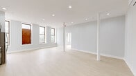Located at 9 Broadway in the heart of downtown Troy, New York, this single-floor unit offers a thoughtfully renovated interior with a clean, modern aesthetic throughout. The open main living area is generously proportioned, featuring light-toned hardwood-style flooring, recessed ceiling lighting, and white structural columns that add an architectural character while preserving the sense of openness. A wall-mounted mini-split system provides climate control. Multiple tall, wood-framed windows allow abundant natural light and frame direct views of Troy's historic downtown streetscape, including nearby monuments and classic masonry buildings.

The kitchen is well-appointed with two-tone cabinetry—white upper cabinets paired with gray-blue lower cabinets—white subway tile backsplash, light stone countertops, and a full suite of stainless steel appliances including a refrigerator, range, and over-the-range microwave. A dedicated bedroom features corner windows that maximize natural light and views of the surrounding urban neighborhood. The bathroom is finished with marble-look tile on both the floors and walls, a white vanity with matte black fixtures, and a clean, bright overall presentation. The unit's neutral light gray walls and consistent flooring unify the space with a cohesive, contemporary feel.