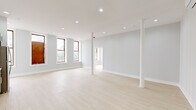 Located at 9 Broadway in the heart of downtown Troy, New York, this single-floor unit offers a thoughtfully renovated interior with a clean, modern aesthetic throughout. The open main living area is generously proportioned, featuring light-toned hardwood-style flooring, recessed ceiling lighting, and white structural columns that add an architectural character while preserving the sense of openness. A wall-mounted mini-split system provides climate control. Multiple tall, wood-framed windows allow abundant natural light and frame direct views of Troy's historic downtown streetscape, including nearby monuments and classic masonry buildings.

The kitchen is well-appointed with two-tone cabinetry—white upper cabinets paired with gray-blue lower cabinets—white subway tile backsplash, light stone countertops, and a full suite of stainless steel appliances including a refrigerator, range, and over-the-range microwave. A dedicated bedroom features corner windows that maximize natural light and views of the surrounding urban neighborhood. The bathroom is finished with marble-look tile on both the floors and walls, a white vanity with matte black fixtures, and a clean, bright overall presentation. The unit's neutral light gray walls and consistent flooring unify the space with a cohesive, contemporary feel.