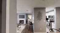 This contemporary apartment showcases a thoughtfully designed layout that maximizes space and functionality. The heart of the home is an open-concept living area, featuring a fireplace with a mounted TV above, creating a cozy focal point. The kitchen boasts white cabinetry, stainless steel appliances, and a breakfast bar that overlooks the living space. The bedroom is adorned with a ceiling fan, large windows, and an en-suite bathroom. Hardwood floors run throughout, complementing the gray walls and modern artwork. Stylish lighting fixtures and carefully chosen furniture pieces enhance the overall aesthetic, resulting in a harmonious and inviting living environment.