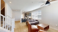 This well-appointed two-story residence offers five bedrooms and six bathrooms across two thoughtfully laid-out floors. The main level features an open-concept kitchen and living area, where light wood-style flooring, neutral white walls, and abundant natural light from multiple windows create a bright, welcoming atmosphere. The kitchen is outfitted with gray shaker-style cabinetry, white quartz countertops, stainless steel appliances including a range, microwave, and refrigerator, and a peninsula with bar seating — ideal for casual dining. Track lighting and a ceiling fan enhance the functional appeal of the main living space. The living area provides comfortable room for seating and entertainment, with large windows fitted with white blinds allowing generous daylight. A smart front door entry with keypad access adds a modern touch. The bedrooms are carpeted and well-sized, each featuring ceiling fans and windows with outdoor greenery views, offering a calm and private retreat. The bathrooms are clean and modern, featuring white vanities with quartz countertops, black matte fixtures, and tub-shower combinations. Additional highlights include multiple closets, hallways connecting the layout efficiently, and a staircase connecting both floors. The overall design is contemporary and functional, suited for multi-occupant living.