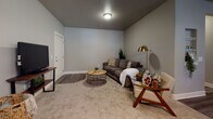 This single-floor residence offers a cohesive layout connecting key living spaces through consistent design elements, including warm hardwood-style flooring and neutral taupe and gray wall tones throughout. The kitchen is well-equipped with dark cabinetry contrasted by white countertops, stainless steel appliances — including a refrigerator, range, microwave, and dishwasher — and a window that brings in natural light. A dedicated dining area adjacent to the kitchen features hardwood-style flooring, a chandelier overhead, and dual windows fitted with blinds. The living room offers a comfortable, relaxed atmosphere with carpet flooring, a ceiling-mounted light fixture, and ample space for seating arrangements. A laundry area is conveniently accessible from the main hallway, which also provides a clear sightline to the kitchen. Two bedrooms feature carpeted floors and windows with blinds; one includes a ceiling fan. Both bathrooms are finished with dark vanity cabinetry and white countertops atop wood-look tile flooring. One bathroom includes a walk-in shower, while the other provides a toilet and vanity. The overall design maintains a clean, modern aesthetic throughout.