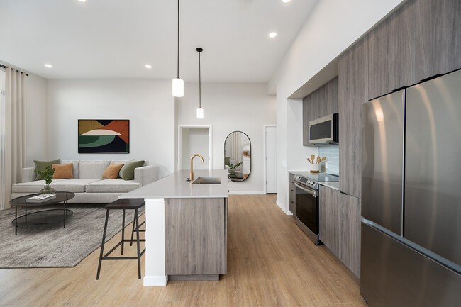 Signature Collection kitchen with dark cabinetry, marbled quartz countertops and backsplash, upgraded stainless steel appliances, and pendant lighting. - Avalon Governors Park