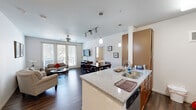 This well-appointed 2-bedroom, 2-bathroom residence in Austin, Texas offers a thoughtfully designed single-level layout. The open-concept living and kitchen area serves as the heart of the home, where dark hardwood flooring flows seamlessly throughout. The kitchen is equipped with stainless steel appliances — including a refrigerator, range, and microwave — warm wood cabinetry, and a generous granite-topped island with a dual basin sink and pendant lighting overhead. A dedicated dining area connects the kitchen to the living room, which is brightened by natural light from large French doors that open to a private balcony with outdoor views. A ceiling fan and track lighting add to the functional design of the living space. The primary bedroom offers a comfortable, carpeted retreat with ample space, while the second bedroom features a window and ceiling fan. Both bathrooms are finished with wood cabinetry, white countertops, and dark hardwood flooring. A closet provides additional storage. The clean, neutral palette and modern finishes throughout create a cohesive and inviting atmosphere, ideally situated in the vibrant East Austin neighborhood.