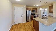 This single-floor residence offers a thoughtfully designed open-concept layout that connects the kitchen, dining, and living areas in a cohesive, functional flow. The kitchen is a standout feature, equipped with rich medium-toned wood cabinetry, granite-look countertops, and a full suite of stainless steel appliances including a refrigerator, electric range, and built-in microwave. A double-basin stainless steel sink sits within a peninsula that provides a natural division between the kitchen and the main living space, accented by a pendant light overhead. In-unit washer and dryer hookups are conveniently tucked nearby.

The living area is generously proportioned, bathed in natural light from large sliding glass doors fitted with vertical blinds that open to an outdoor view. Warm hardwood-style flooring extends throughout the common areas, lending a cohesive, inviting feel. Bedrooms are carpeted for comfort, with one featuring a ceiling fan and another offering access to a spacious walk-in closet. The bathroom is finished with a wood vanity, granite-look countertop, and a walk-in shower with safety grab bars. Throughout the residence, neutral-toned walls and consistent finishes create a clean, welcoming ambiance.