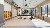 Located at 5180 Peachtree Blvd in Chamblee, GA, this professionally designed fitness facility offers a generously sized, single-floor exercise space thoughtfully divided into distinct training zones. The open-concept layout features soaring ceilings with exposed ductwork and sleek linear lighting, creating a modern industrial ambiance throughout.

The strength training area is equipped with power racks, cable machines, a full dumbbell rack, kettlebells, medicine balls, and a heavy punching bag, all set on durable rubberized flooring. An artificial turf lane runs through the center of the space, ideal for functional and athletic training drills. Mirror-clad columns and walls enhance the sense of openness while allowing members to monitor form.

A dedicated cycling studio features rows of stationary spin bikes on smooth hardwood-style flooring, a large-screen display, ceiling fans, and built-in bench seating with locker storage along the walls. Natural light streams in through large windows flanked by exposed brick walls, adding warmth and texture to the environment.

The facility also includes treadmills, ellipticals, and additional cardio equipment positioned for visibility and accessibility. Multiple mounted flat-screen TVs are distributed throughout the space, keeping members engaged during workouts. The overall design balances high-performance functionality with a polished, inviting aesthetic.