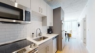Located at 1450 N Dayton Street in Chicago's Lincoln Park/Old Town neighborhood, this single-floor unit showcases a contemporary industrial-modern aesthetic defined by exposed concrete ceilings throughout and warm light wood flooring that creates a cohesive visual flow across all rooms.

The kitchen is efficiently designed with white subway tile backsplash, crisp white quartz countertops, and gray cabinetry accented with gold-toned hardware. Stainless steel appliances—including an electric range, over-the-range microwave, dishwasher, and full-size refrigerator—complete the functional space, which opens directly toward a dining area bathed in natural light.

The living area is a standout, featuring floor-to-ceiling windows that frame sweeping urban views of Chicago's skyline, allowing abundant natural light to fill the space and highlight the clean, minimalist design.

Multiple bedrooms feature the same exposed concrete ceilings and wood flooring. Each includes closet space, and select rooms offer direct window access with city views, lending an airy, open character to the private quarters.

The bathroom is finished with gray cabinetry, a white vanity countertop, and a white subway tile shower surround, maintaining the unit's consistent modern palette throughout.