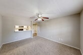This single-floor residence offers a practical and comfortable layout comprising a combined kitchen and living room, one bedroom, one bathroom, and a hallway. The galley-style kitchen is well-appointed with white cabinetry, light-toned countertops, a stainless steel sink with a matte black faucet, and black appliances including an electric range and refrigerator. Wood-look flooring runs throughout the kitchen, giving it a clean, modern feel. A pass-through opening connects the kitchen to the living area, enhancing the sense of openness between the two spaces. The living room is bright and welcoming, featuring soft carpet flooring, neutral wall tones, a ceiling fan with integrated lighting, and a large window that allows generous natural light and outdoor views. The bedroom is a comfortable retreat, carpeted and well-sized, with a prominent window framing views of surrounding greenery. It provides direct access to the bathroom, as well as an additional door to a closet or secondary space. The bathroom is equipped with a full-size tub and shower combination finished in white tile, complemented by clean, simple fixtures. Throughout the residence, a consistent neutral color palette and practical finishes create a cohesive and functional living environment.