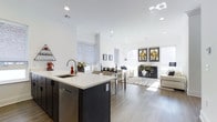 This single-floor space at 278A showcases a thoughtfully designed open-concept layout that integrates the kitchen, dining, and living areas into one cohesive, flowing environment. The interior is finished in a crisp, all-white palette across the walls and ceilings, complemented by recessed lighting that ensures consistent, even illumination throughout.

The kitchen features a substantial dark-toned island with a white quartz countertop and an undermount sink with a modern brushed-nickel faucet. Dark cabinetry provides strong contrast against the light surroundings, while stainless steel appliances add a contemporary, functional edge. The island offers additional storage and serves as a natural transition point into the dining area.

The dining space accommodates a full table and seating arrangement, framed by roller shades on multiple windows that allow natural light to filter in softly. Beyond, the living area is generously proportioned, with large windows that invite abundant daylight. Light hardwood-style flooring runs continuously throughout, unifying the space and contributing to its open, airy character. A curated art display and neutral furnishings complete the welcoming, modern ambiance.